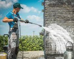 A person power-washing a brick wall